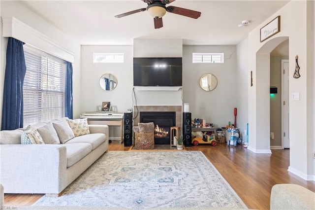 living area featuring wood finished floors, arched walkways, a fireplace, baseboards, and ceiling fan