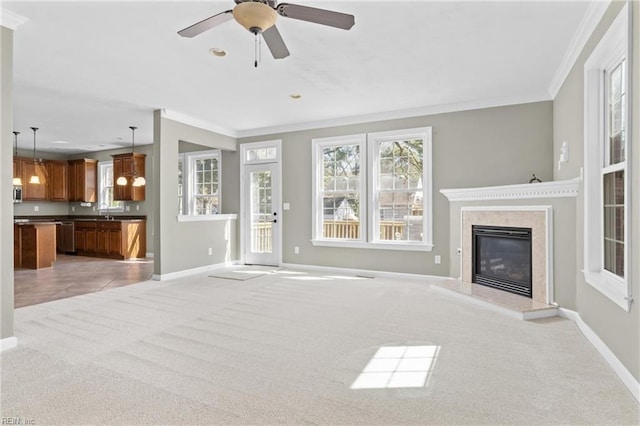 unfurnished living room with a ceiling fan, baseboards, a high end fireplace, ornamental molding, and light carpet