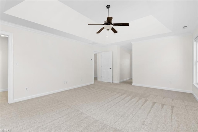 empty room with crown molding, baseboards, light carpet, a raised ceiling, and a ceiling fan