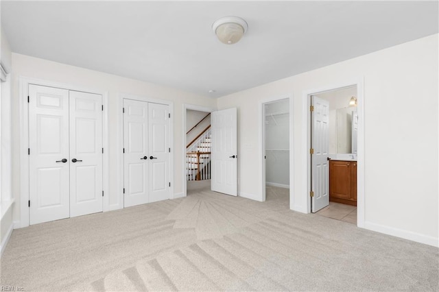 unfurnished bedroom with two closets, baseboards, ensuite bathroom, and light carpet