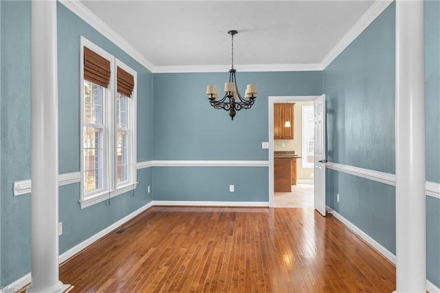 empty room with a notable chandelier, a healthy amount of sunlight, wood-type flooring, and ornamental molding