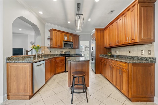 kitchen featuring visible vents, ornamental molding, a kitchen island, stainless steel appliances, and brown cabinetry