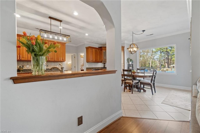 kitchen featuring baseboards, arched walkways, hanging light fixtures, crown molding, and tasteful backsplash