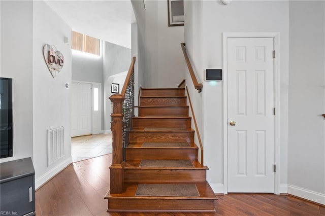 stairs featuring visible vents, baseboards, wood finished floors, and a towering ceiling