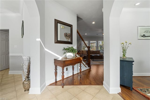 corridor with arched walkways, crown molding, tile patterned flooring, baseboards, and stairs