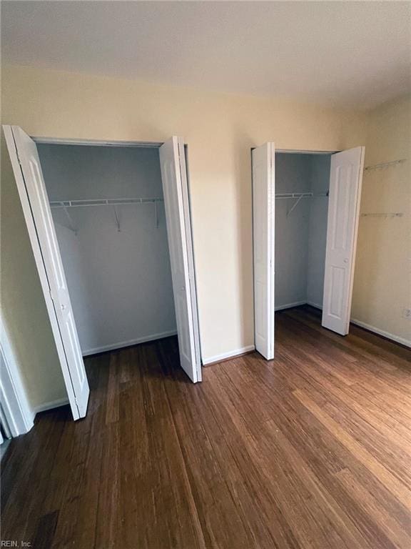 unfurnished bedroom with baseboards, multiple closets, and wood finished floors