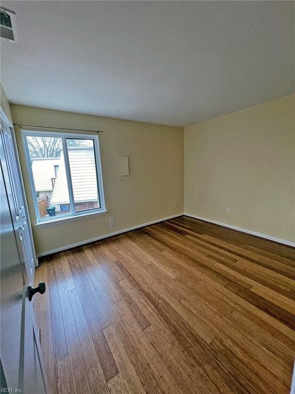 empty room with wood finished floors, visible vents, and baseboards