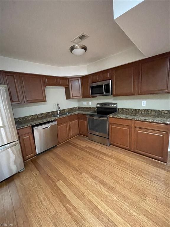 kitchen featuring visible vents, dark stone counters, a sink, stainless steel appliances, and light wood-type flooring