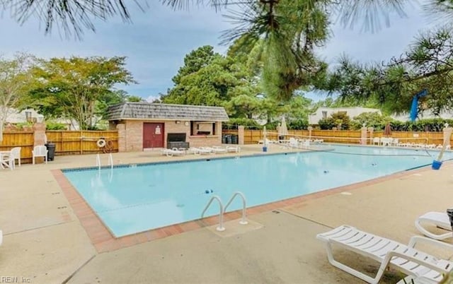 community pool with a patio, an outdoor structure, and fence