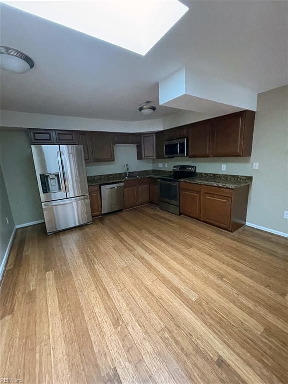 kitchen with stainless steel appliances, baseboards, light wood-style floors, and a skylight