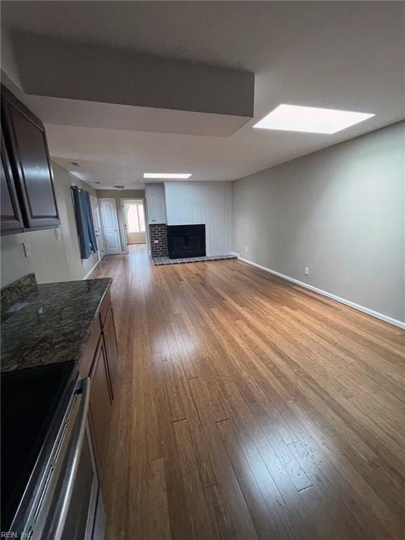 unfurnished living room featuring a fireplace with raised hearth, a skylight, baseboards, and wood-type flooring