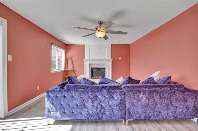 living room with ceiling fan, a large fireplace, baseboards, and wood finished floors