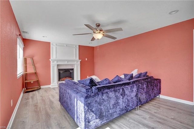 living room featuring a fireplace, wood finished floors, baseboards, and a ceiling fan