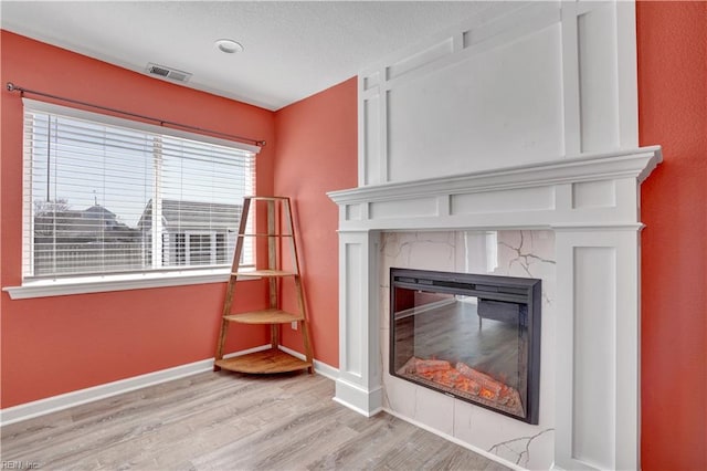 room details featuring a high end fireplace, visible vents, baseboards, wood finished floors, and a textured ceiling