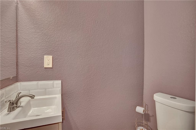 bathroom featuring vanity, toilet, and a textured wall