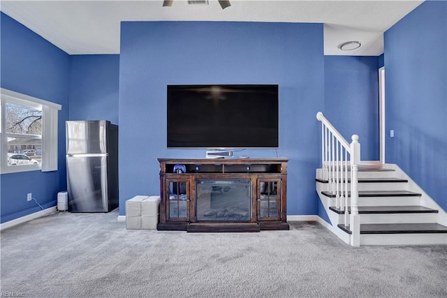 unfurnished living room with visible vents, ceiling fan, baseboards, stairway, and carpet flooring