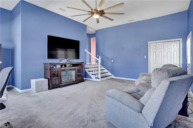 living room featuring visible vents, baseboards, stairway, carpet flooring, and a ceiling fan