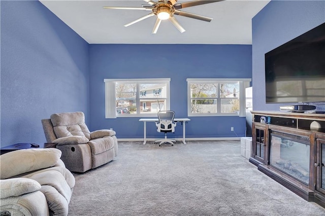 living room with a glass covered fireplace, baseboards, carpet, and a ceiling fan