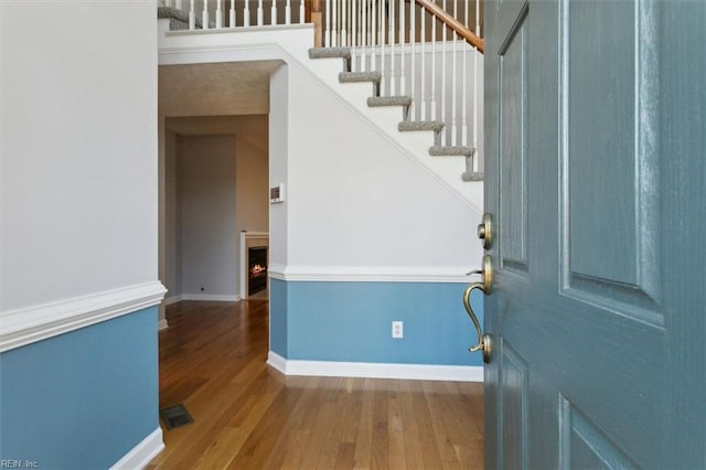 foyer entrance featuring visible vents, a warm lit fireplace, baseboards, and wood finished floors