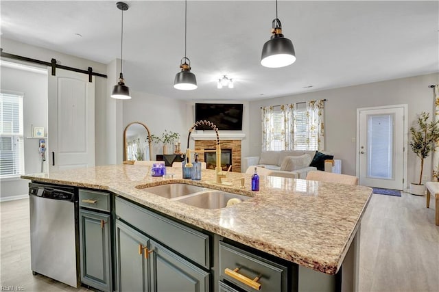 kitchen featuring a center island with sink, a sink, light wood-style floors, dishwasher, and a barn door