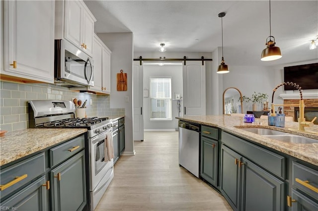 kitchen with a sink, white cabinetry, a barn door, appliances with stainless steel finishes, and decorative backsplash