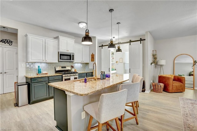 kitchen featuring light wood finished floors, backsplash, a barn door, appliances with stainless steel finishes, and a sink