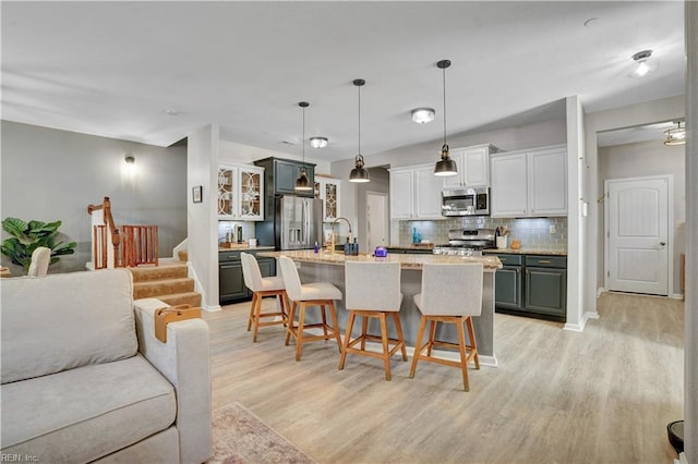 kitchen with glass insert cabinets, a breakfast bar area, light wood-type flooring, decorative backsplash, and stainless steel appliances