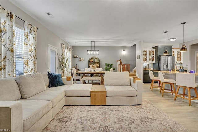 living area with light wood finished floors, visible vents, a chandelier, and stairs