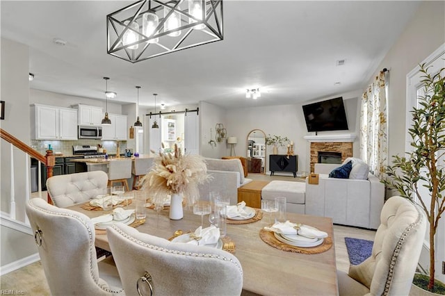 dining room featuring a barn door, baseboards, a stone fireplace, and stairway