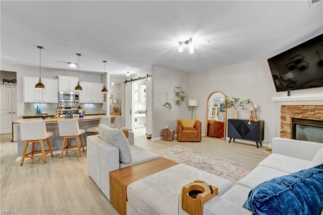 living room featuring a stone fireplace, a barn door, light wood-style floors, and baseboards