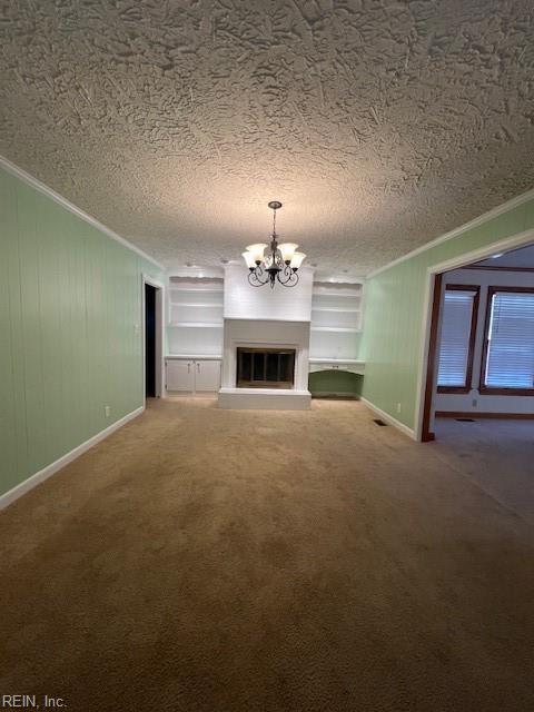 unfurnished living room featuring carpet floors, ornamental molding, a textured ceiling, a glass covered fireplace, and a chandelier