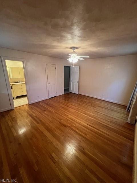 unfurnished bedroom featuring ensuite bath, a ceiling fan, baseboards, and wood finished floors