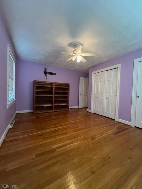 unfurnished bedroom with ceiling fan, baseboards, two closets, and wood finished floors