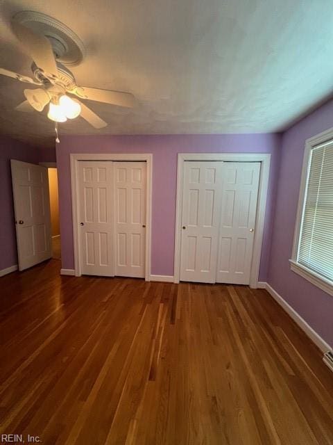 unfurnished bedroom featuring wood finished floors, baseboards, and multiple closets