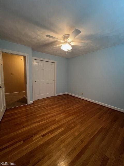 unfurnished bedroom with dark wood finished floors, baseboards, a closet, and ceiling fan