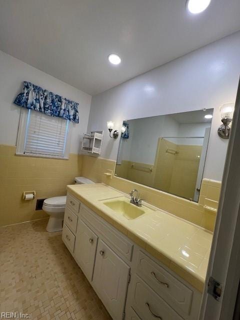 bathroom featuring toilet, a stall shower, tile walls, wainscoting, and vanity