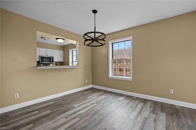 unfurnished dining area with baseboards and dark wood-style flooring