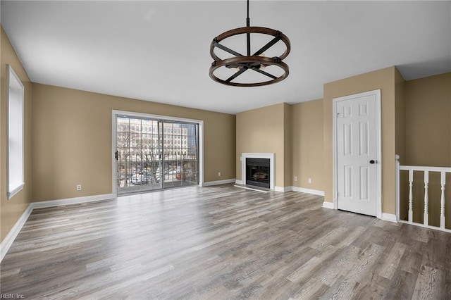 unfurnished living room with a fireplace with raised hearth, baseboards, and wood finished floors