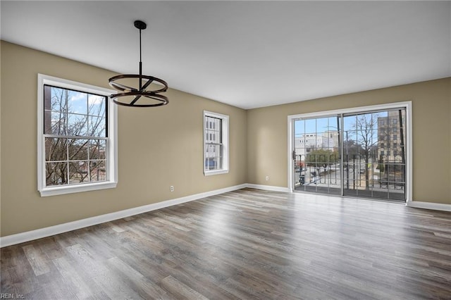 unfurnished room featuring an inviting chandelier, wood finished floors, and baseboards