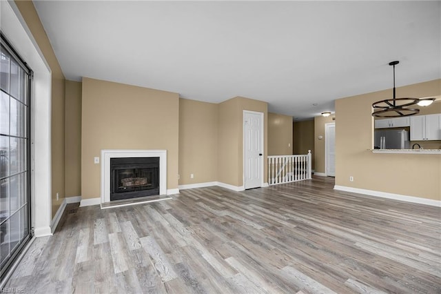 unfurnished living room with wood finished floors, baseboards, and a fireplace with raised hearth