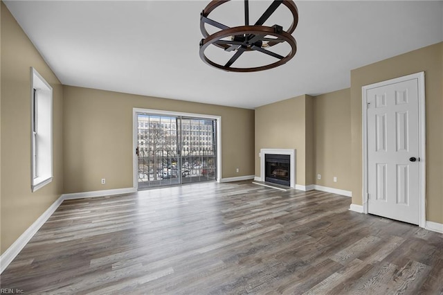 unfurnished living room with a glass covered fireplace, plenty of natural light, baseboards, and wood finished floors