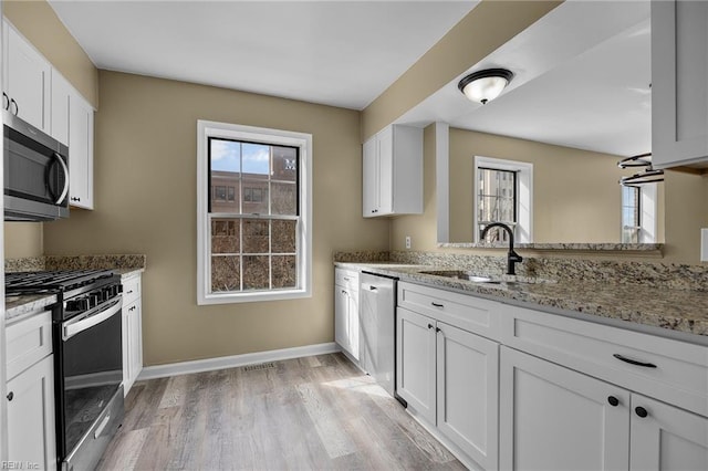 kitchen featuring light stone countertops, baseboards, a sink, white cabinets, and appliances with stainless steel finishes