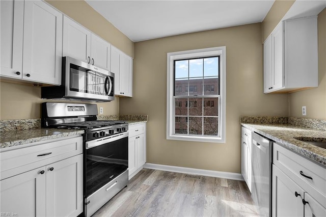 kitchen featuring light stone counters, stainless steel appliances, baseboards, and white cabinets