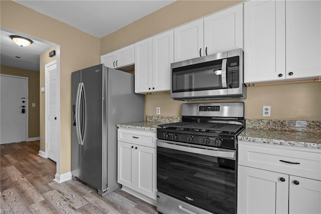 kitchen with light wood-type flooring, white cabinetry, appliances with stainless steel finishes, baseboards, and light stone countertops