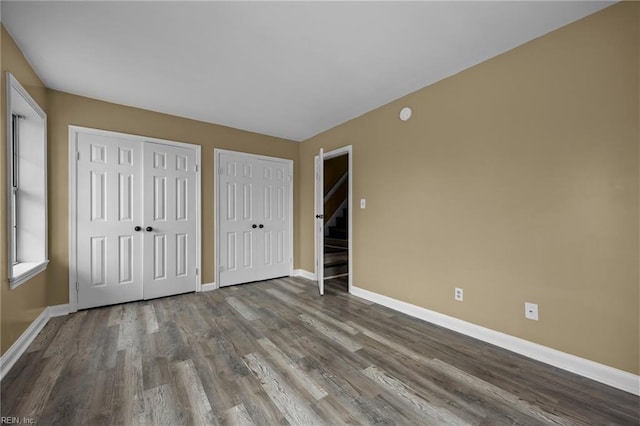 unfurnished bedroom with wood finished floors, baseboards, and two closets