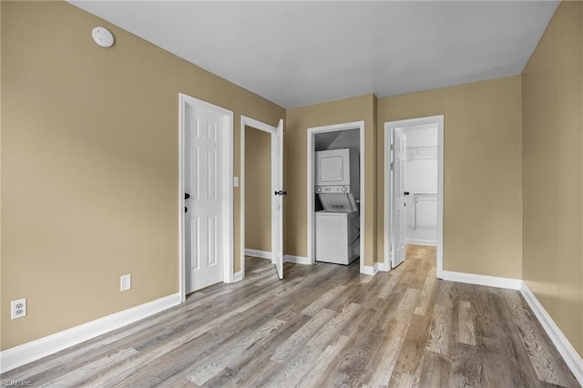 unfurnished bedroom with a closet, wood finished floors, baseboards, and stacked washer and dryer