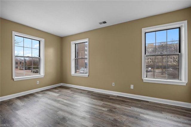 unfurnished room featuring wood finished floors, a healthy amount of sunlight, visible vents, and baseboards