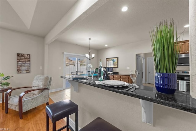 kitchen featuring light wood finished floors, appliances with stainless steel finishes, pendant lighting, a kitchen breakfast bar, and a notable chandelier