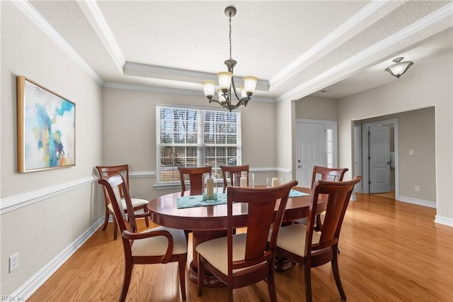 dining area featuring a raised ceiling, crown molding, a notable chandelier, and light wood-style floors