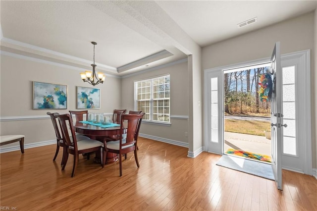 dining area featuring light wood-type flooring, visible vents, a notable chandelier, ornamental molding, and a tray ceiling